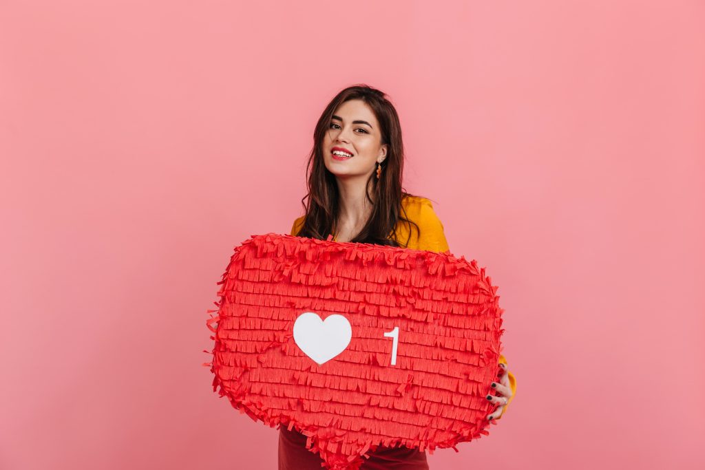teenager girl bright outfit is smiling holding red like sign from instagram pink wall min 1 1024x683 - 2024’s Latest Guide On Watching Instagram Stories Anonymously!